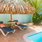 Tropical poolside lounge area at Wayaca Oasis Retreat in Aruba with shaded palapa and relaxing sun chairs